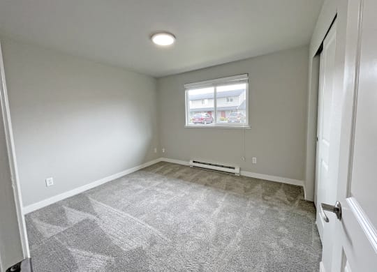 Bedroom with gray carpet, window with white blinds on the back wall, on right wall double sliding door closet.at Quilceda Gardens, Marysville, 98270