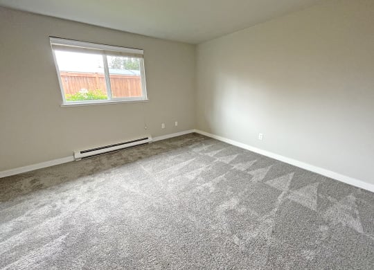 Light-filled bedroom corner, gray carpet, a large window on the left wall with heater below.at Quilceda Gardens, Marysville, 98270