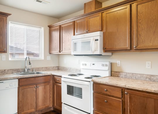 Corner of the kitchen with a dishwasher, sink, oven, and microwave from left to right. Wooden cabinets and a light-filled window on the left wall. at Pine Tree Park, Washington, 99337