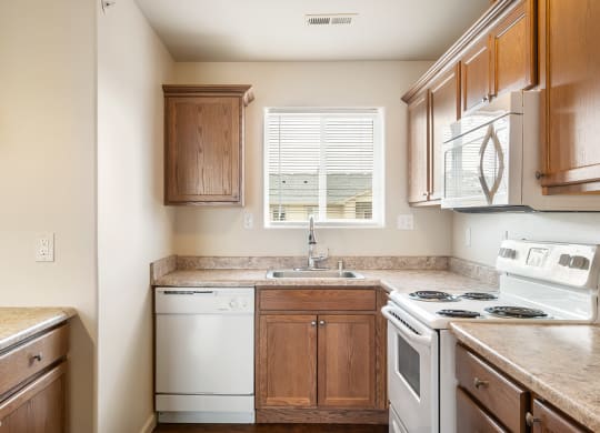 L-shaped kitchen with breakfast bar to the left and white appliances including a dishwasher, stove, oven, microwave, and sink with window above. at Pine Tree Park, Washington
