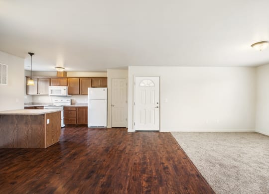a kitchen and living room with hardwood floors and white walls. Living area carpeted with large window on the right wall. at Pine Tree Park, Kennewick