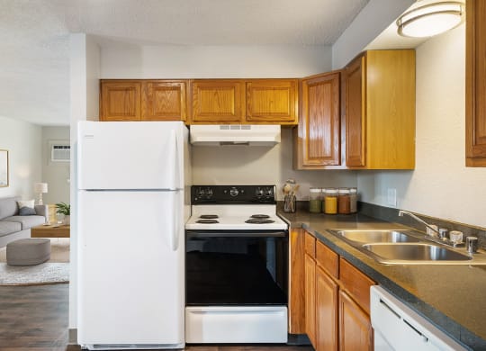 A side view of the kitchen with a white full-size refrigerator next to a stovetop oven and wood cabinets.at Wildflower, Kennewick, 99336