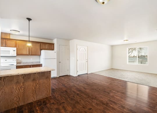 A kitchen with hardwood floors looking into the carpeted living room, with a front door between. A large window is on the right wall. at Pine Tree Park, Kennewick