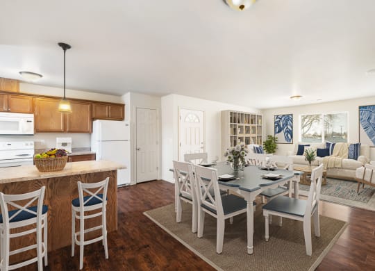 Kitchen opens up to the dining area and living room. Staged with dining set, couch, two chairs, wall bookshelf, and rugs. at Pine Tree Park, Washington