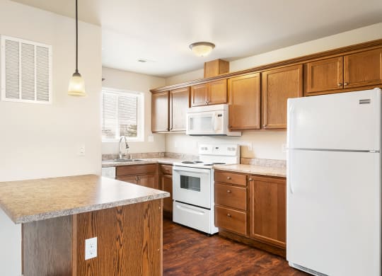 A kitchen with wood cabinets, hardwood floorings, white appliances, and a light-filled window above the sink. at Pine Tree Park, Kennewick, WA
