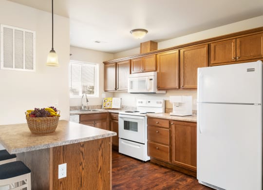 L-shaped kitchen with top and bottom cabinet storage, white appliances, and a breakfast bar staged with bar stools. at Pine Tree Park, Kennewick