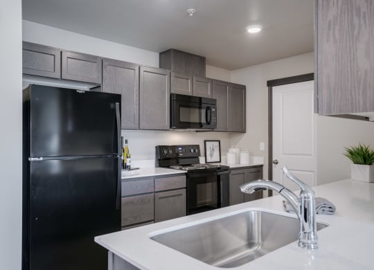 Kitchen with white countertops and grey cabinets. Kitchen has black fridge, black stove and oven, black microwave and stainless steel sink. at Altitude, East Wenatchee, WA, 98802