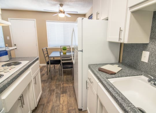 Galley kitchen with new white cabinets and gray faux granite countertops, with dining area visible in the distance at Woodland Village , California, 95695