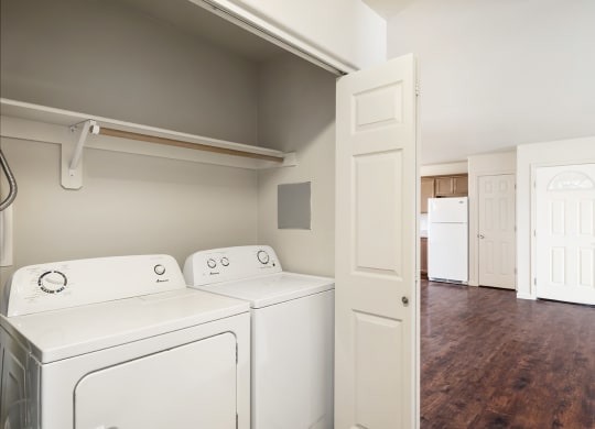 A laundry closet with accordion doors, a white washer and dryer, and shelf storage above. at Pine Tree Park, Washington