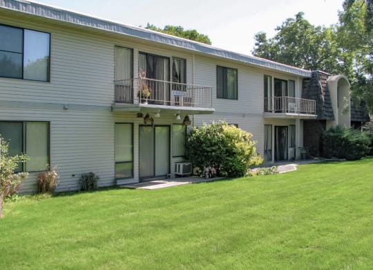 Exterior apartments with large windows, balconies, large patios surrounded by manicured grass, landscaping, and trees behind.at Laurel Park, Idaho