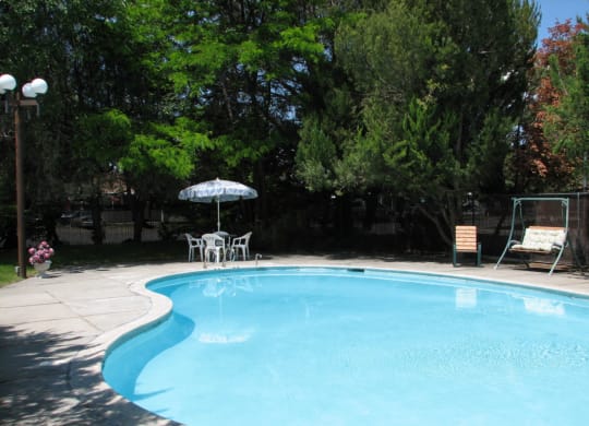 Swimming pool with umbrella seating, swing bench, surrounded by manicured lawn and large green trees.at Laurel Park, Twin Falls
