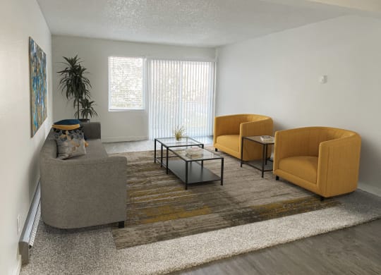 Carpeted living room, large window, sliding glass doors to balcony on back wall, staged with 2 orange chairs, couch, coffee table.at Laurel Park, Twin Falls, ID