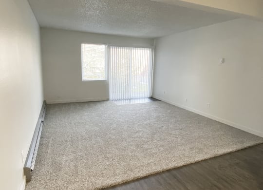 Open living room with gray carpets, a window, and sliding glass door to balcony with nature views on the back wall.at Laurel Park, Twin Falls, Idaho