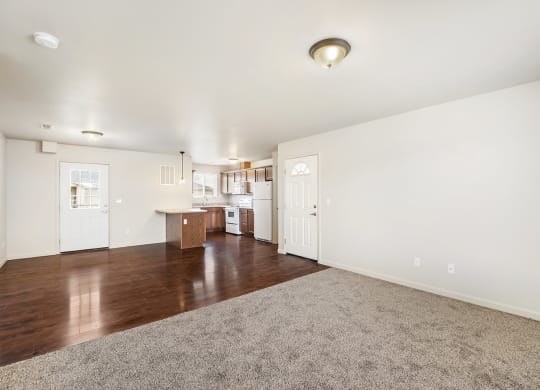 The living room has white walls and a gray carpet that meets hardwood floors in the dining area and kitchen. at Pine Tree Park, Kennewick