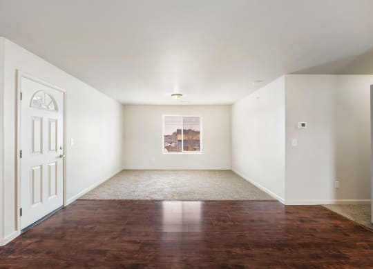 Clean, bright living room and entry space. Entry has dark faux wood flooring, and living room has taupe carpeting. There is a window in the living room wall. at Pine Tree Park, Kennewick, WA