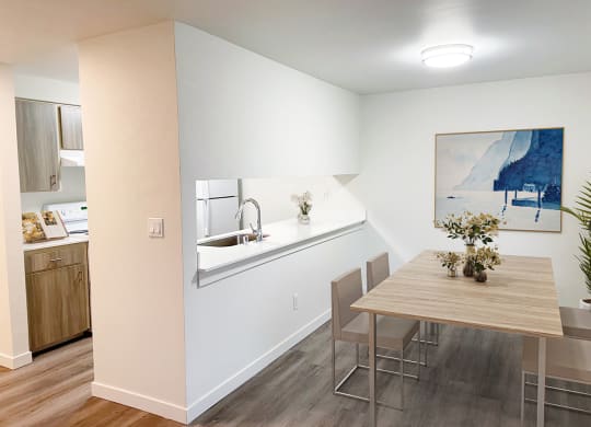 Apartment kitchen and dining area with white walls and wood floors. Staged with a dining table, chairs and art.at The Trail, Washington, 98290