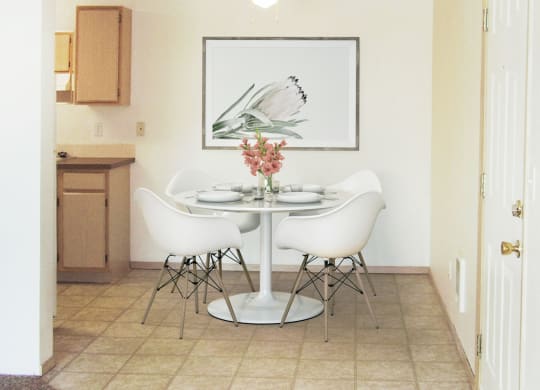 Dining area with ceiling fan, and the kitchen to the left. Staged with a table, 4 chairs, wall art, and flowers.at North Pointe, Post Falls Idaho