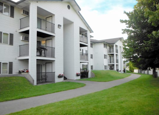 North Pointe Apartments exterior with covered patios and balconies surrounded by fenced green grass, a paved path, and trees.at North Pointe, Post Falls