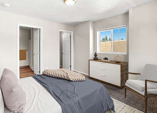 A bedroom with a bed, chair, and a window with a view of a field in Post Falls, ID Apartments.