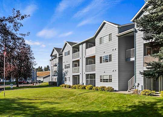 The Overlook Apartments in Post Falls with open green space and trees in front of the building.