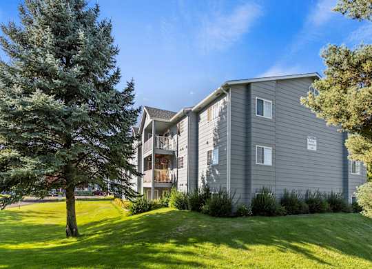 Grey apartment building at The Overlook Apartments in Post Falls with a large grassy lawn and trees.
