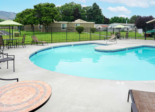 Curved outdoor pool with chairs and tables and a fence around it.at Park View Apartments, Wenatchee, WA 98801