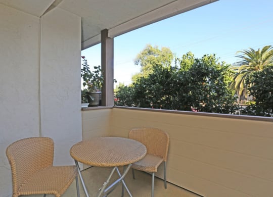 Apartment private patio with small table and two chairs overlooking trees on a sunny day at Pacific Sands, California, 92117