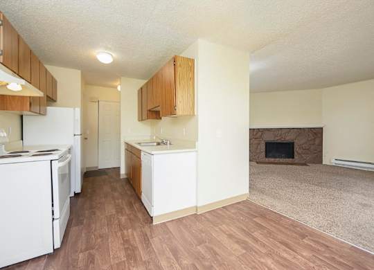 Kitchen with wood-like flooring separated by a wall from carpeted living room with fireplace and mantle.