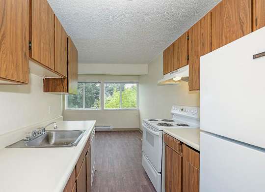 Double galley kitchen, wood cabinet storage, white countertops, and appliances. Full-size fridge, dishwasher, oven, stove top.