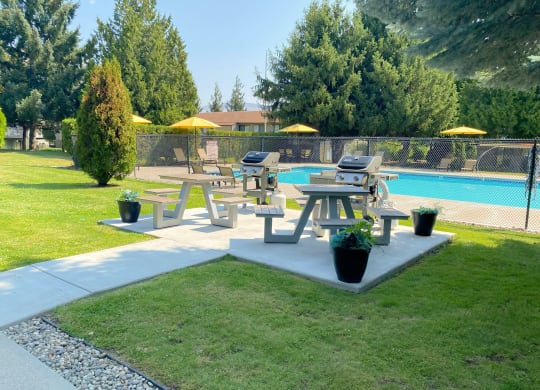a picnic table sits on a concrete slab in a grassy area next to a swimming pool at Cedarwood, Wenatchee, 98801