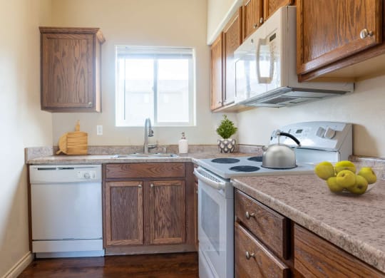 L-shaped kitchen with wood cabinets top and bottom, dishwasher, sink with window above, oven, stovetop, microwave. at Pine Tree Park, Washington, 99337