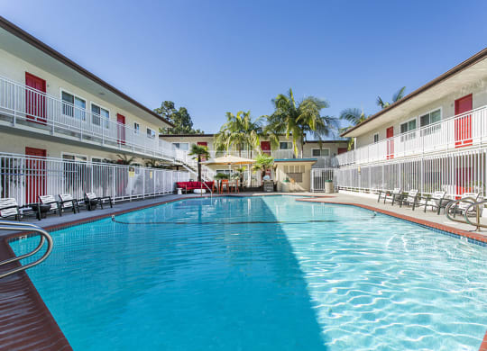 Outdoor swimming pool with sun chairs, a lounge area lined with apartments, and palm trees at Pacific Sands, San Diego, CA