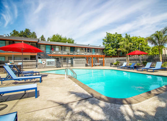 Woodland Village pool with blue lounge chairs, red umbrellas and landscaping.at Woodland Village Apartments , Woodland