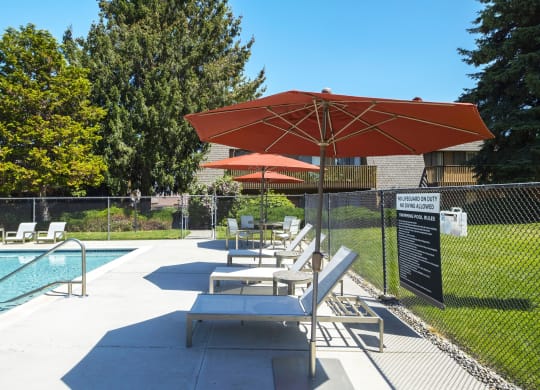 Community pool with lounge chairs and orange umbrellas surrounded by grass at Castlerock, Wenatchee