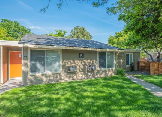 A Park View apartment home with an orange door and a yard with green grass, trees and a private patio.at Park View Apartments, Wenatchee, WA