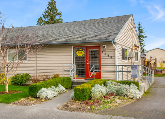 Outside of Leasing Office, red doors, a 'Now Leasing' sign, a wheelchair ramp,  landscaping, basketball court behind. at Quilceda Gardens, Washington