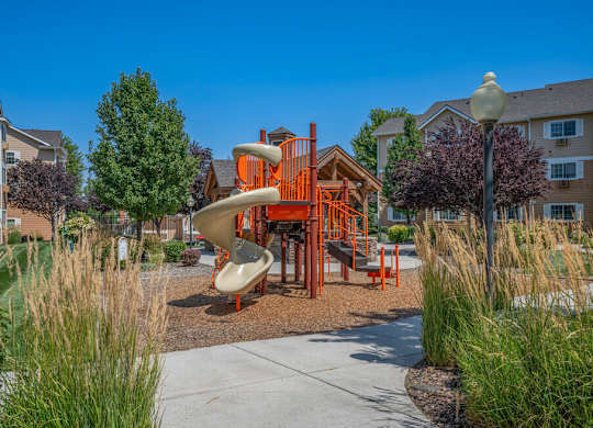 A playground with a slide and a play structure in the middle of a grassy area.