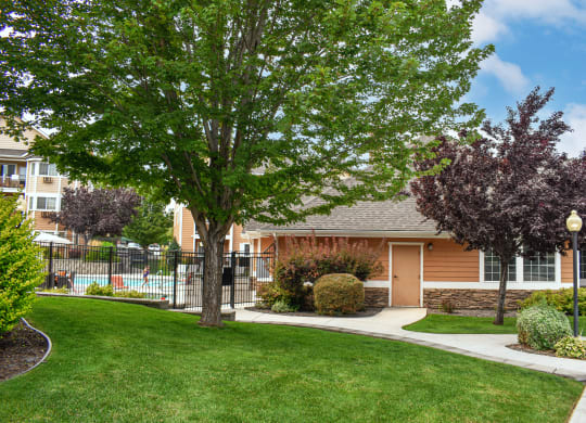 Exterior of community with green grass, trees and a pool in the background.