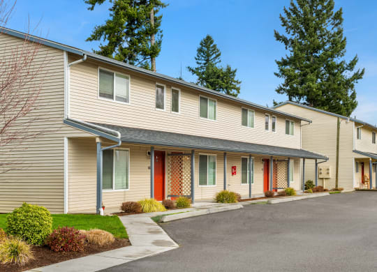 Exterior apartments lined with a paved walkway, maintained landscaping, trees in the distance, and parking spaces in front.at Quilceda Gardens, Marysville, WA 98270