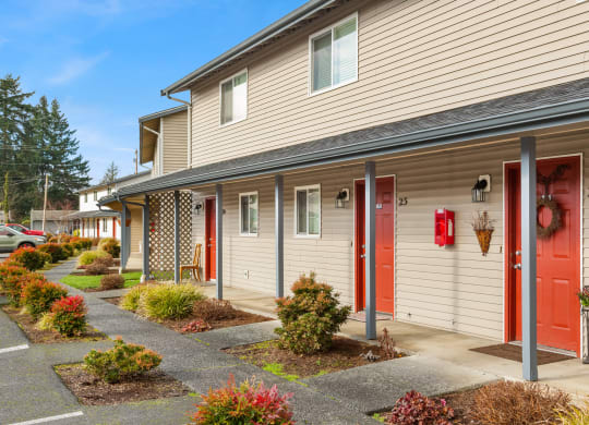 Outside apartments with red doors and paved walkways with colorful landscaping leading to each door.at Quilceda Gardens, Marysville, WA