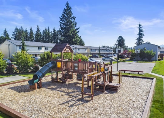 Large outdoor community playground with green slide, surrounded by manicured lawn with full basketball court behind.at Quilceda Gardens, Marysville, WA
