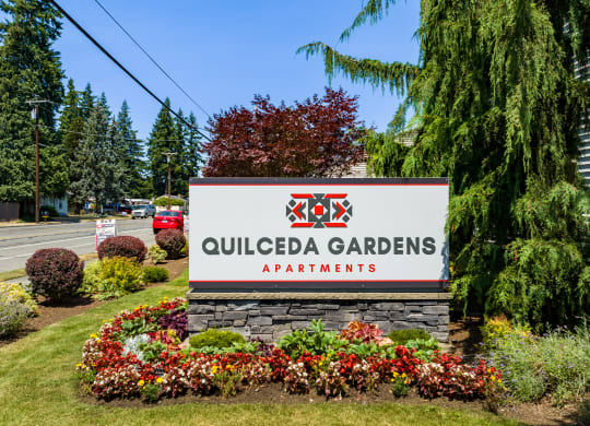 a sign for Quilceda Gardens Apartments in front of trees and flowers