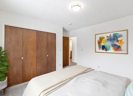 A bedroom with a bed, a painting, and a plant.