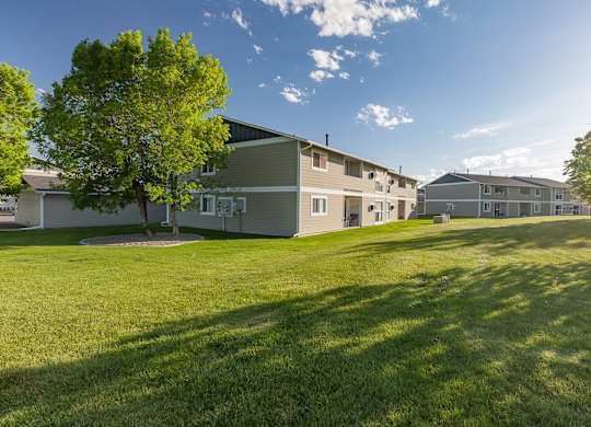 Row of apartments in Billings, MT with a large grass field and trees surrounding buildings
