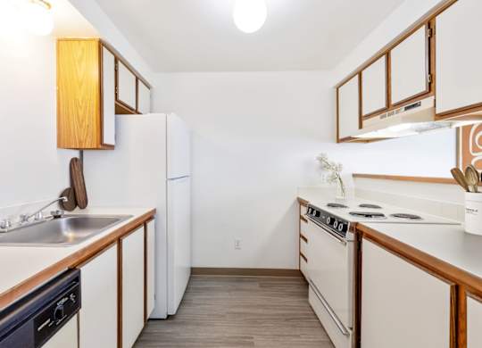 A double galley kitchen with white appliances and wooden cabinets at Shiloh Glen Apartments in Bilings.