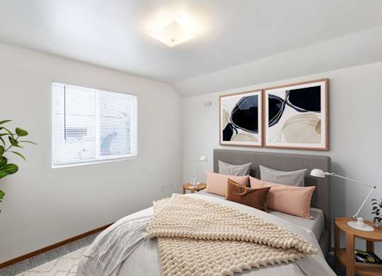 A bedroom with a bed, pillows, a plant, and a painting on the wall at Shiloh Glen Apartments in Billings, MT.