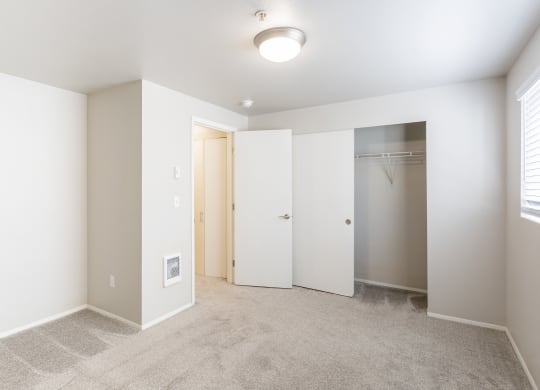 an empty bedroom with a closet and a window and beige carpet at Sitka Heights in Fife