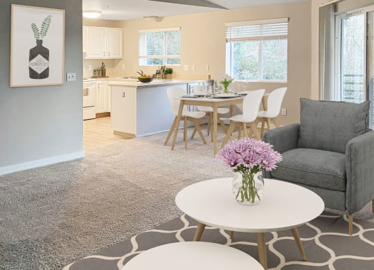 Open living room with sliding doors to a private balcony on left and kitchen in back. Staged with coffee tables, chair, dining set.at Sitka Heights, Washington