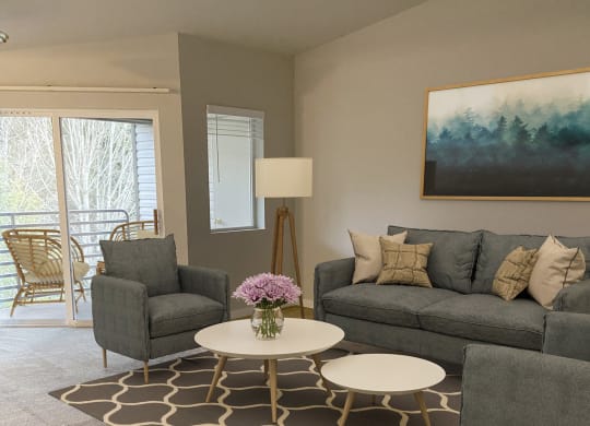 Living room with large sliding glass doors to private covered patio. Staged with 2 chairs, a couch, coffee tables, lamp.at Sitka Heights, Fife Washington
