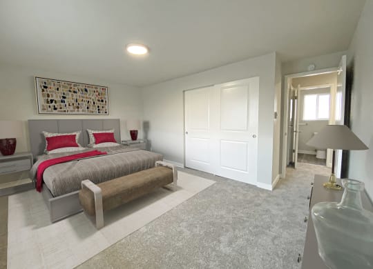 Bedroom with gray carpet, double door closet, opening to hallway. Staged with a queen-sized bed, tables, art, dresser.at Quilceda Gardens, Washington, 98270